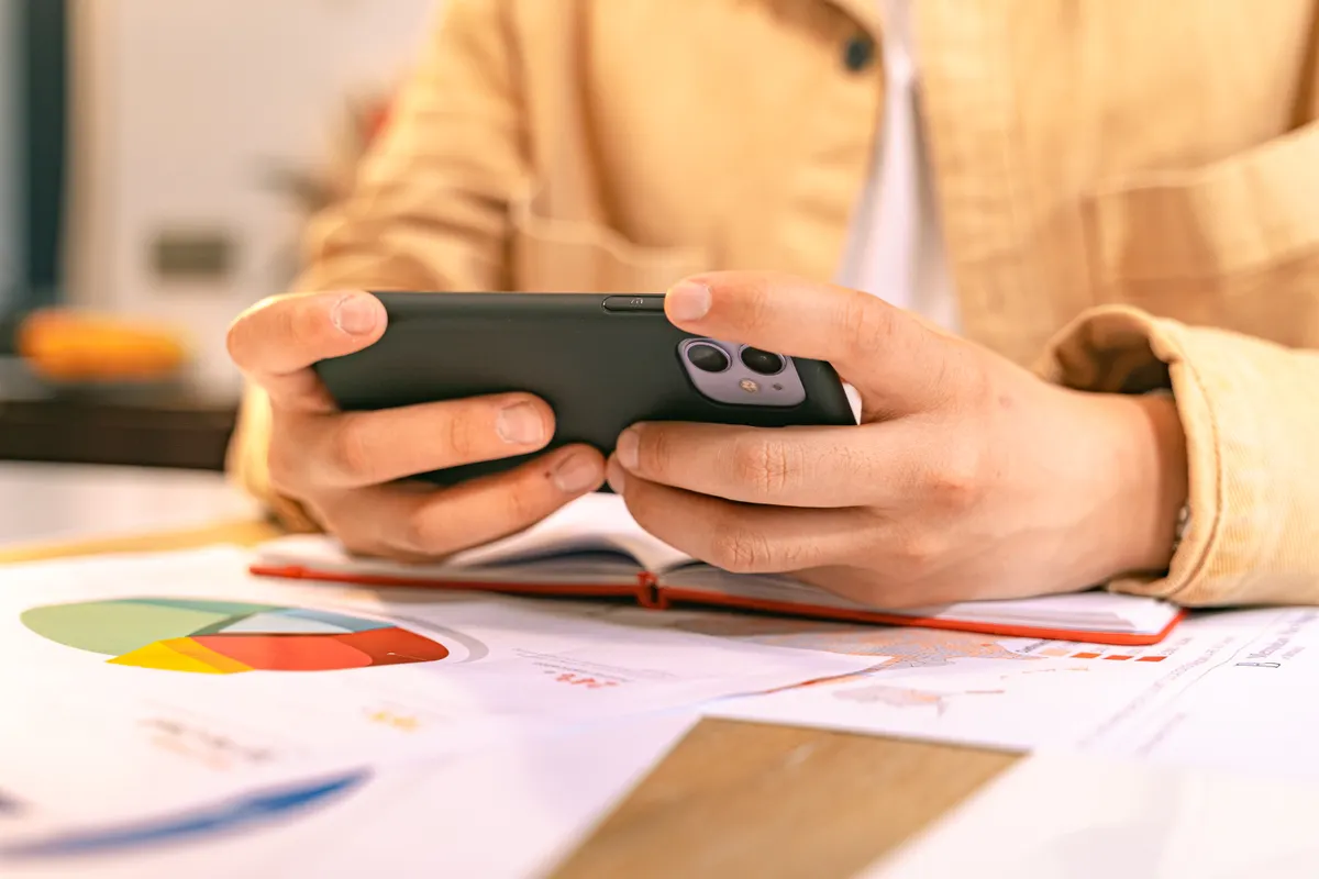 Person reviewing information at a desk with a smartphone and open notebook.