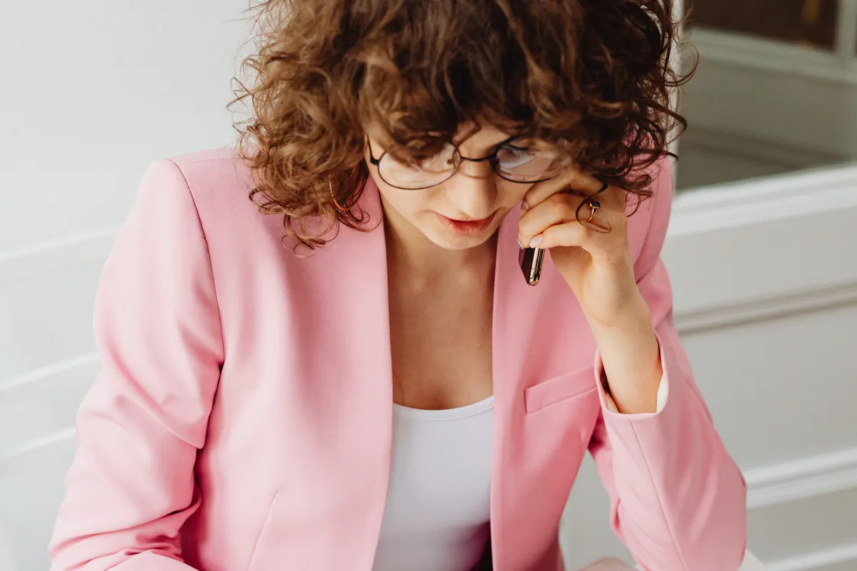 Woman wearing glasses and a pink jacket speaking on a mobile phone.
